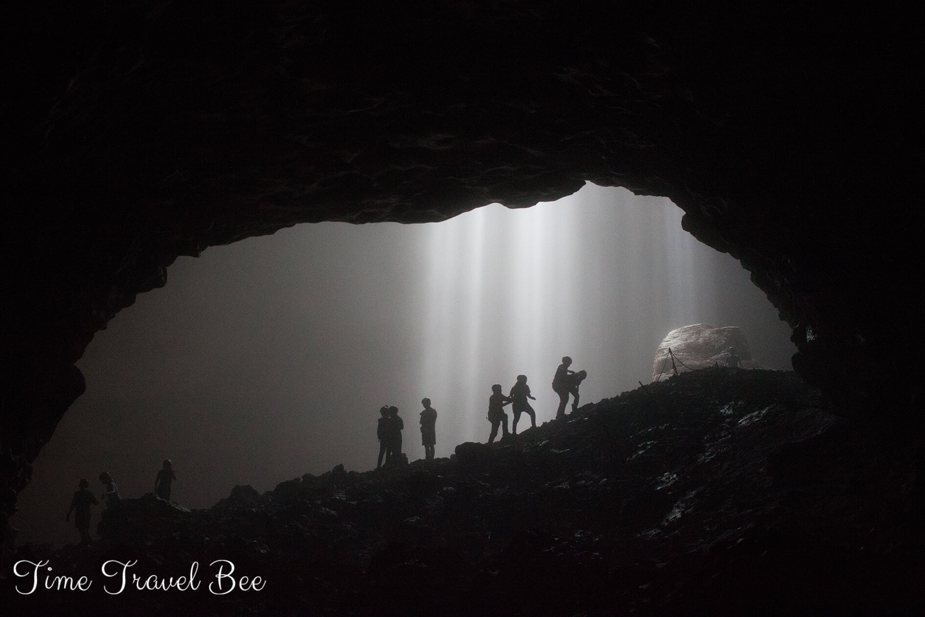 People climbing the cave and light coming from the hole.