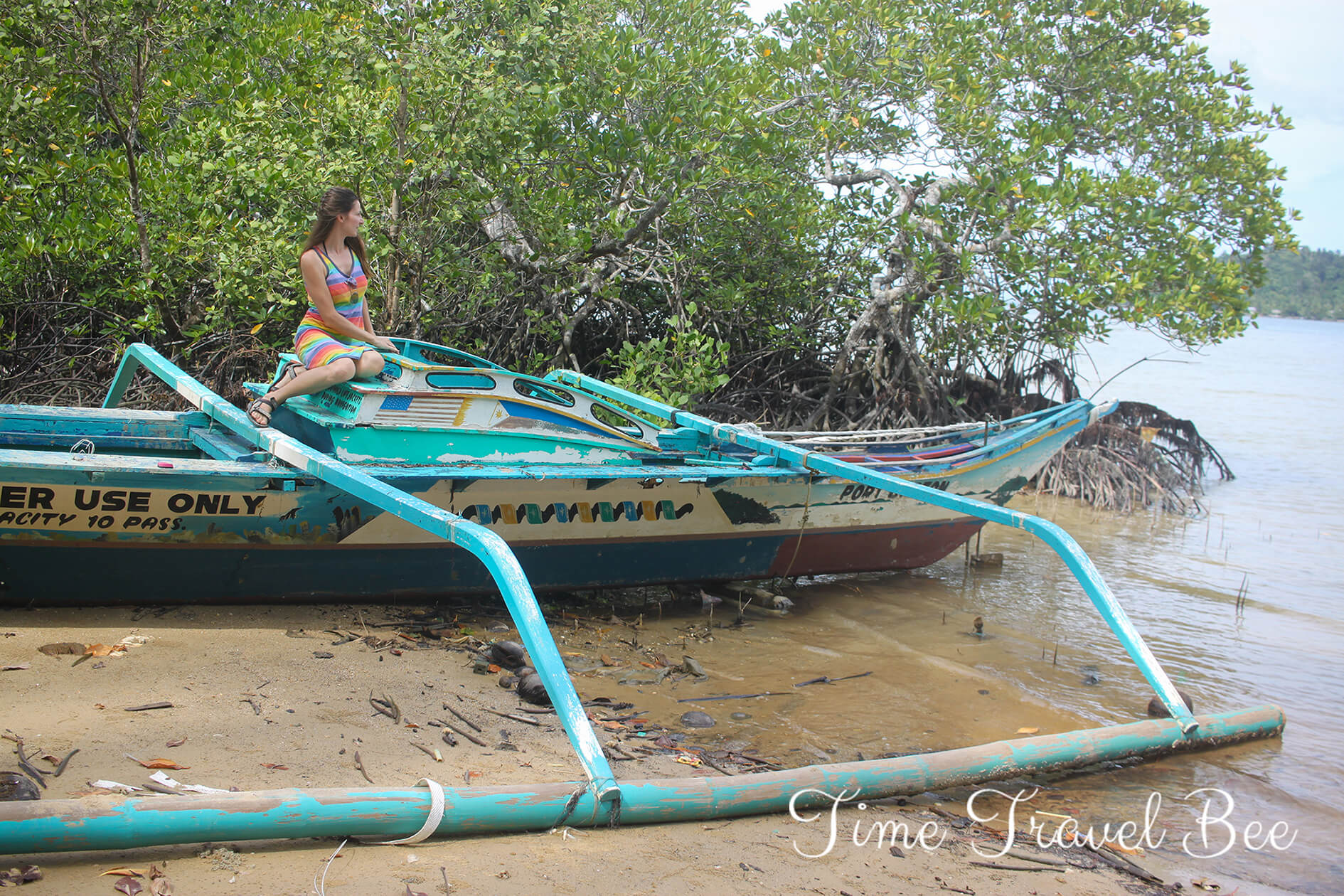 Girl sitting on the old boat in Port Barton. Blue boat with bamboo stilts.