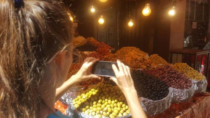 Bazar w Oranie. Dziewczyna robi zdjęcia telefonem oliwkom śródziemnomorskim.